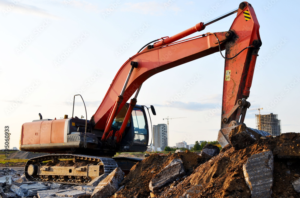 Large tracked excavator works in a gravel pit. Loading of stone and rubble for its processing at a concrete factory into cement for construction work. Cement production factory on mining quarry Large tracked excavator works in a gravel pit. Loading of stone and rubble for its processing at a concrete factory into cement for construction work. Cement production factory on mining quarry