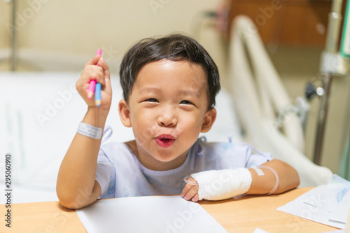 The patient boy is painting the paper with a color pencil in the hospital.