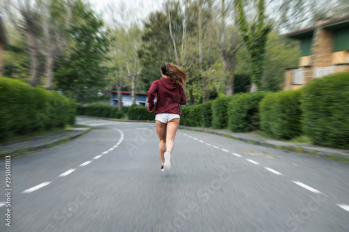 Back view of young female athlete running fast at urban suburbs street road on autumn.