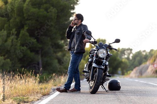 Man biker talking on the phone to the insurance of his motorcycle after having suffered a breakdown on the road.