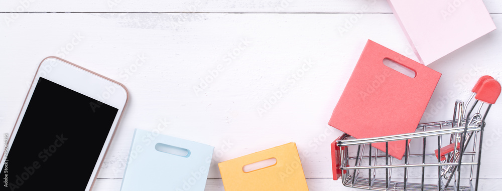 Abstract online shopping, mobile payment concept design element, colorful cart and paper bags on white wooden table background, top view, flat lay Abstract online shopping, mobile payment concept design element, colorful cart and paper bags on white wooden table background, top view, flat lay