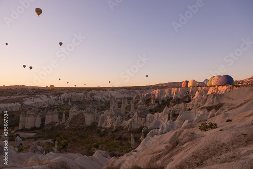 morning photo in Cappadocia with air balloons in the sky and on the ground behind sandy hills