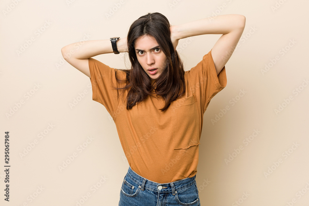 Young brunette woman against a beige background covering ears with hands trying not to hear too loud sound. Young brunette woman against a beige background covering ears with hands trying not to hear too loud sound.