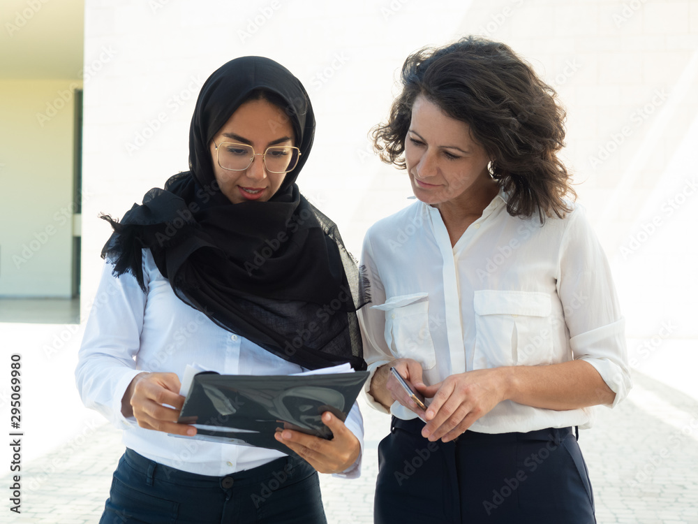 Muslim female professional consulting colleague. Young business woman in hijab showing document to coworker. Expertise concept