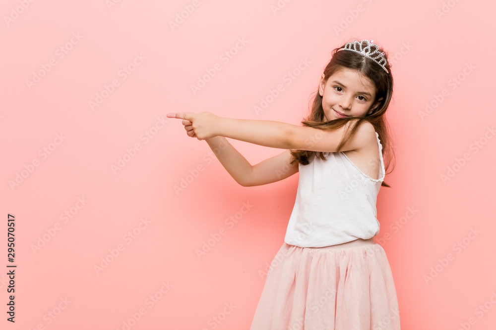 Little girl wearing a princess look excited pointing with forefingers away. Little girl wearing a princess look excited pointing with forefingers away.