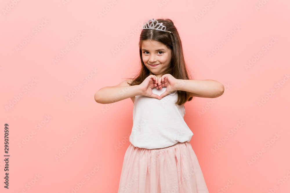 Little girl wearing a princess look smiling and showing a heart shape with hands. Little girl wearing a princess look smiling and showing a heart shape with hands.