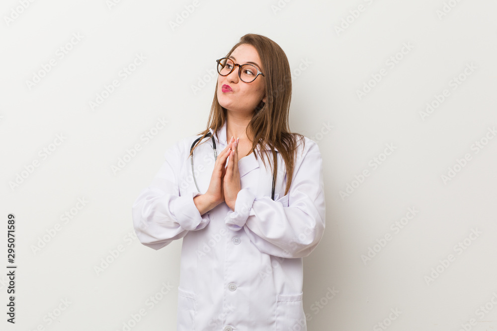 Young doctor woman against a white wall making up plan in mind, setting up an idea. Young doctor woman against a white wall making up plan in mind, setting up an idea.