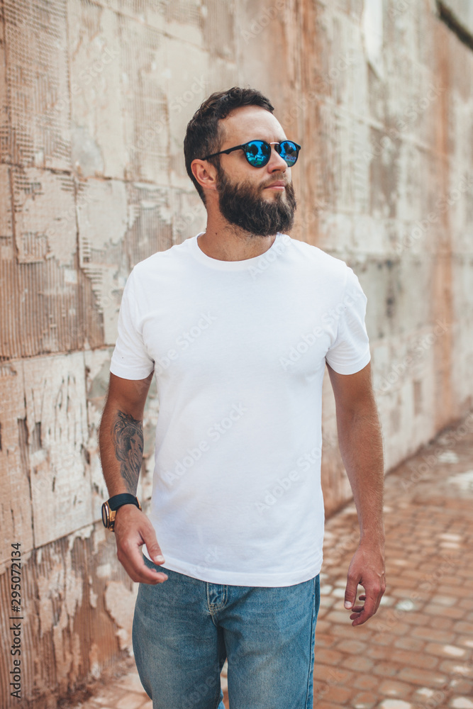 Young hipster man with beard wearing white blank t-shirt and blue jeans outdoor. Young hipster man with beard wearing white blank t-shirt and blue jeans outdoor.