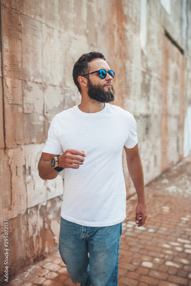 Young hipster man with beard wearing white blank t-shirt and blue jeans outdoor.