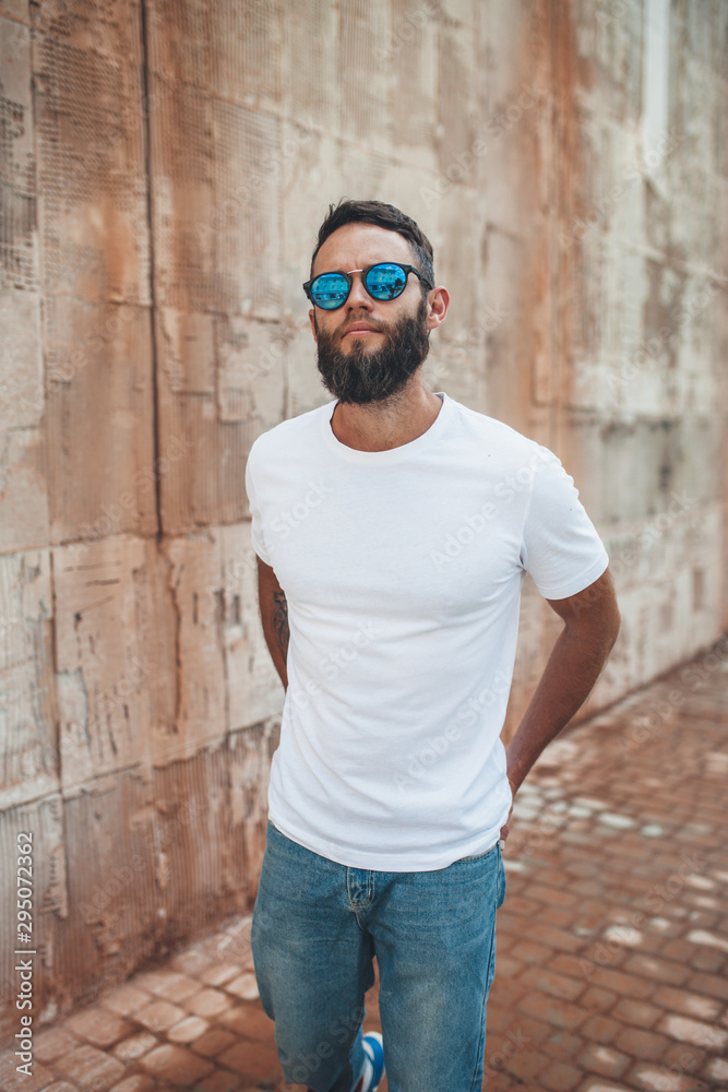 Obraz premium Young hipster man with beard wearing white blank t-shirt and blue jeans outdoor.