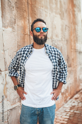 Young hipster man with beard wearing white blank t-shirt and blue jeans outdoor. © San4ezz007