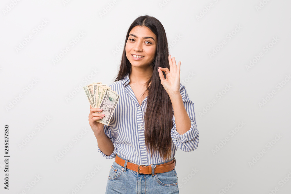 Young arab woman holding dollars cheerful and confident showing ok gesture. Young arab woman holding dollars cheerful and confident showing ok gesture.