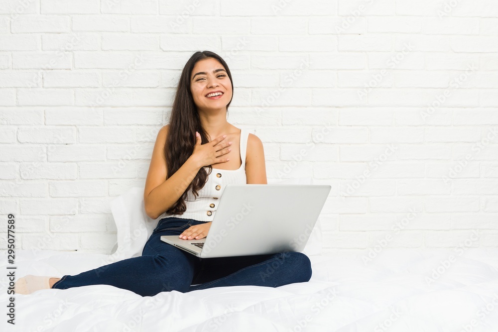 Young arab woman working with her laptop on the bed laughs out loudly keeping hand on chest. Young arab woman working with her laptop on the bed laughs out loudly keeping hand on chest.