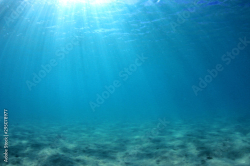 Underwater background of clear blue water on sandy sea floor 