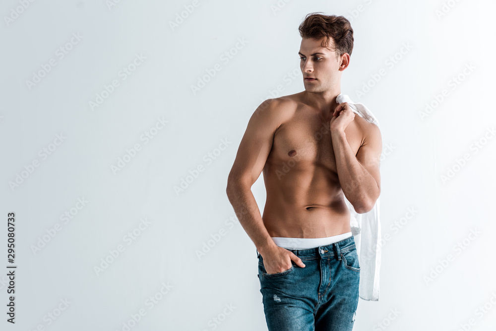 muscular young man in denim jeans standing with hand in pocket and holding shirt isolated on white muscular young man in denim jeans standing with hand in pocket and holding shirt isolated on white