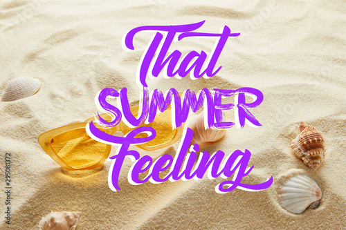 yellow stylish sunglasses on sand with seashells and that summer feeling lettering