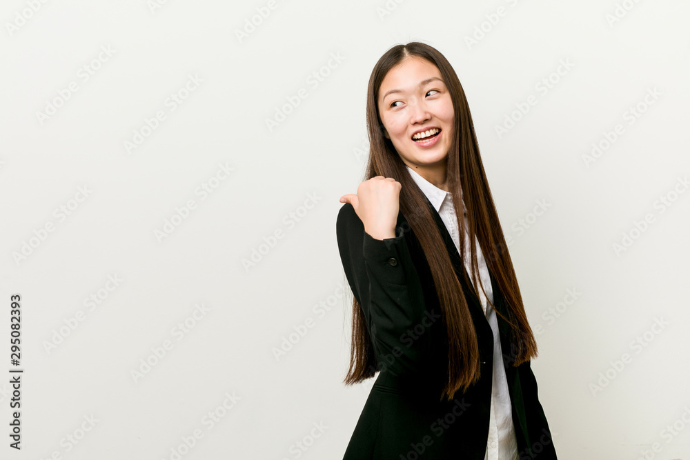 Young pretty chinese business woman points with thumb finger away, laughing and carefree. Young pretty chinese business woman points with thumb finger away, laughing and carefree.