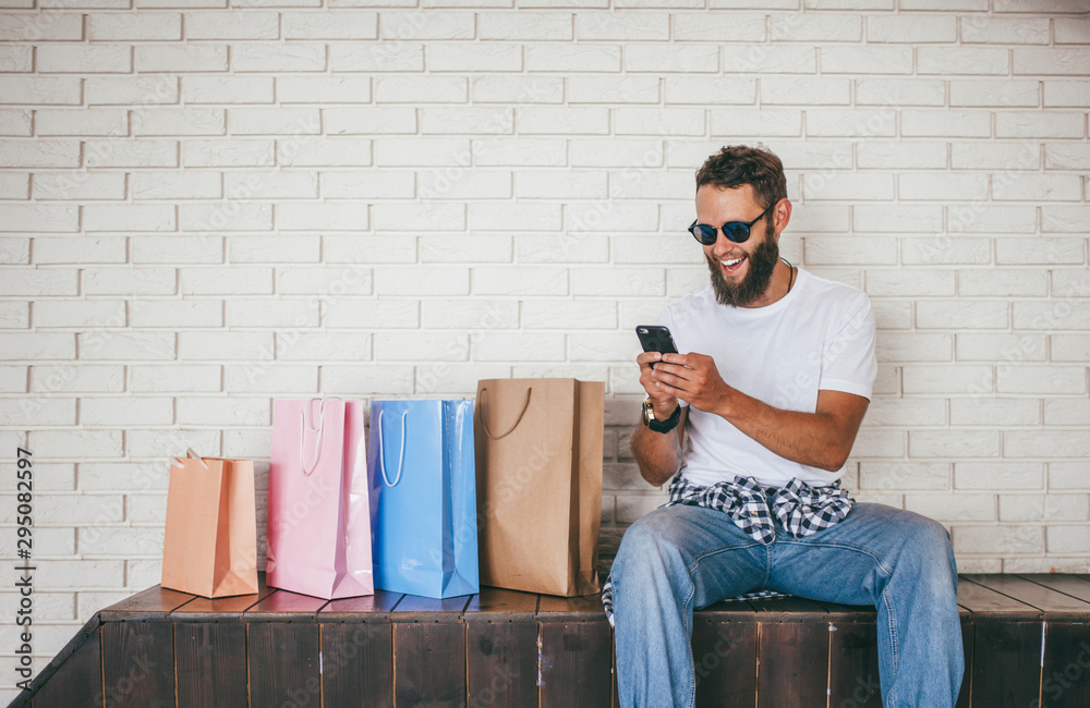 Handsome bearded man doing shopping in an online store., wearing blue jeans  and holding blank craft paper bags with copy space for label . Discount,  sale, season sales. black friday. Stock Photo