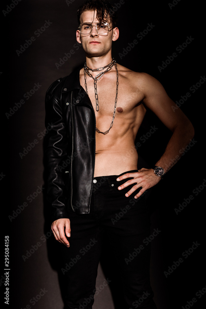muscular man with chains on neck standing with hand on hip on black