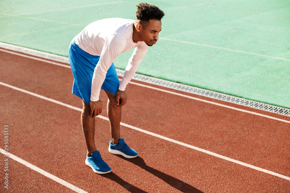 Young tired African American sportsman made a stop during run on racetrack at stadium