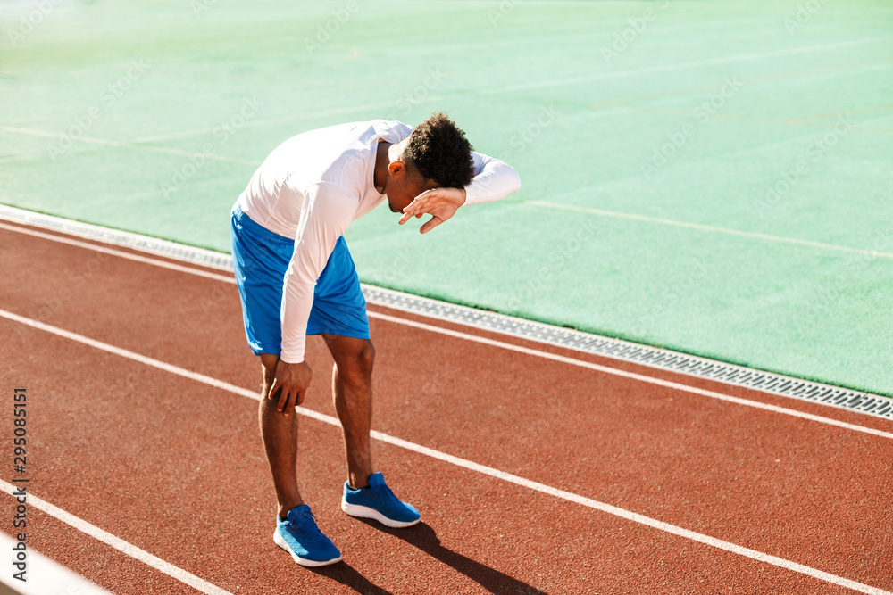 Obraz premium Young exhausted African American sportsman made a stop during run on racetrack at stadium