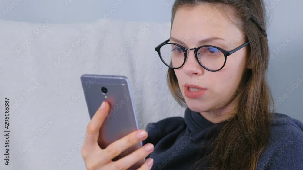 Happy young brunette woman in glasses talk a video chat on a mobile phone sitting in armchair Happy young brunette woman in glasses talk a video chat on a mobile phone sitting in armchair