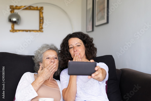 Mother and daughter talking to other relatives through video call. Middle aged woman and elderly lady using smart phone and sending air kiss to screen. Video call concept photo