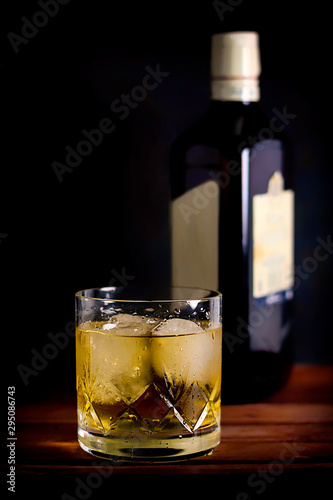 WHISKEY GLASS WITH ICE AND BOTTLE ON DARK FUND