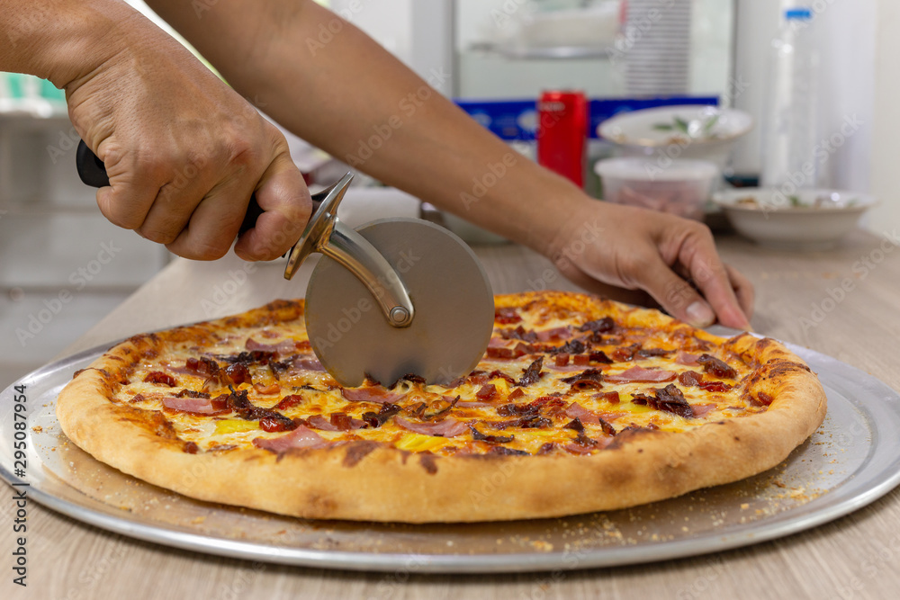 Closeup hand of chef cutting pizza on table.