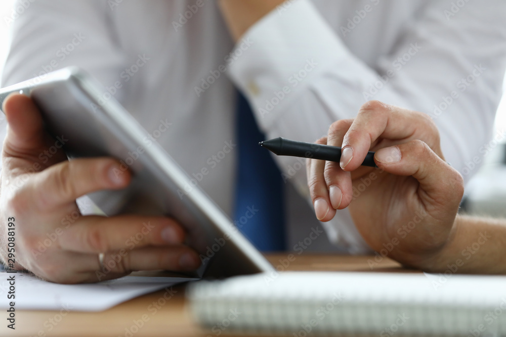 Focus on male hand holding stylos. Colleague with modern tablet explaining conditions of contract. Businessmen discussing new start-up. Business meeting concept. Blurred background Focus on male hand holding stylos. Colleague with modern tablet explaining conditions of contract. Businessmen discussing new start-up. Business meeting concept. Blurred background
