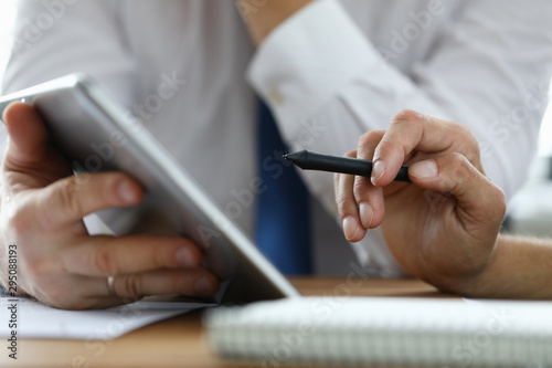 Focus on male hand holding stylos. Colleague with modern tablet explaining conditions of contract. Businessmen discussing new start-up. Business meeting concept. Blurred background © H_Ko