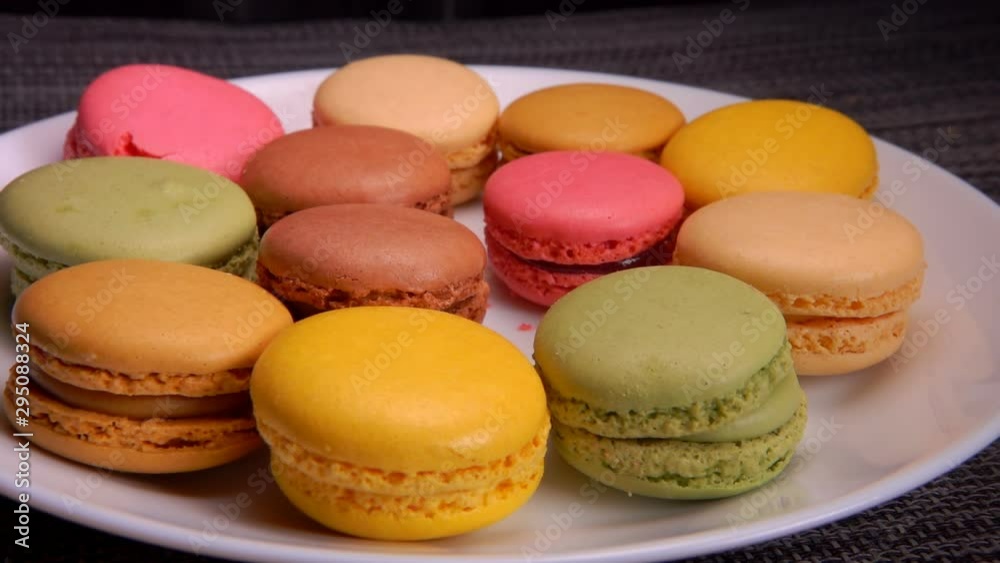 Multi-colored French macaroons lie on a white plate. Many hands take macaroons from a plate Multi-colored French macaroons lie on a white plate. Many hands take macaroons from a plate