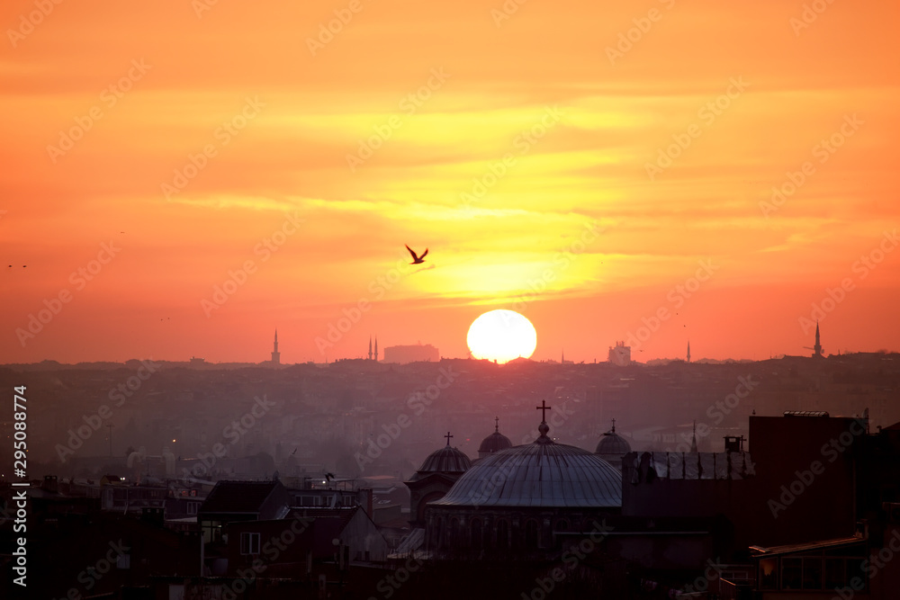 View of Istanbul at sunset. Roofs of old houses, the big sun setting over the horizon, seagulls against the sunset sky. The atmosphere of the ancient city.