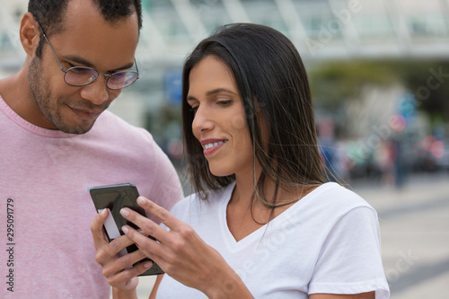 Front view of good friends looking at smartphone. Smiling multiracial colleagues looking at phone on street. Communication and technology concept