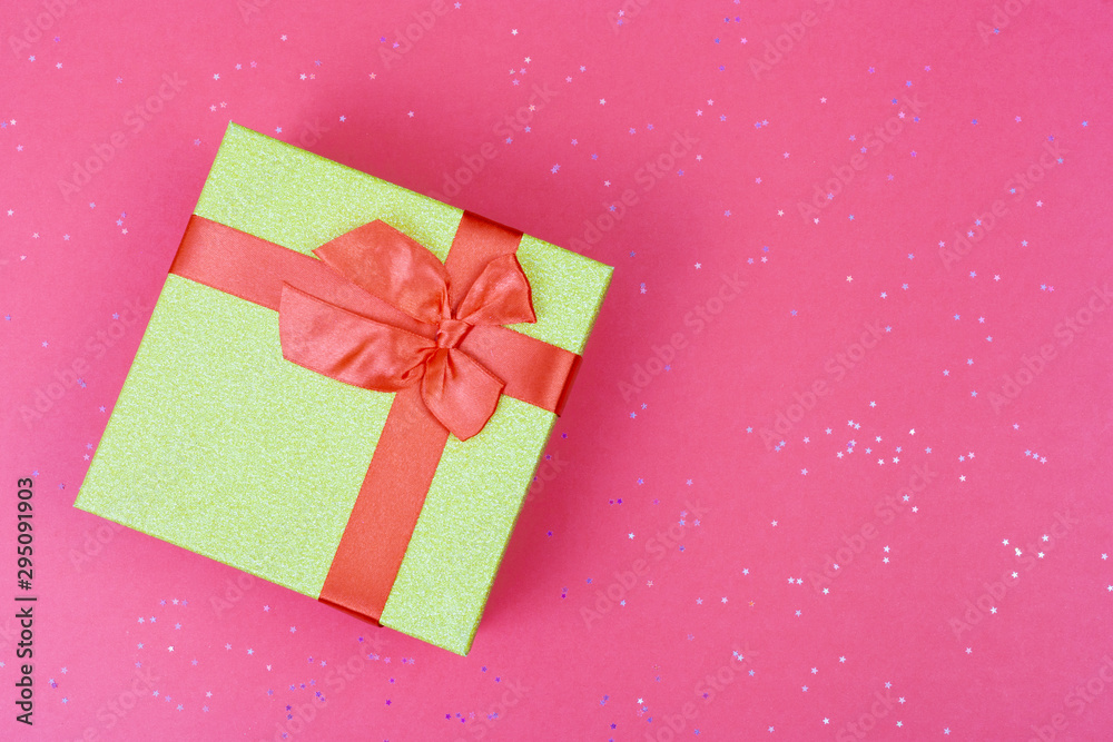 Fototapeta premium Green gift box with bow on trendy colored background with sparkles. Flat lay style.