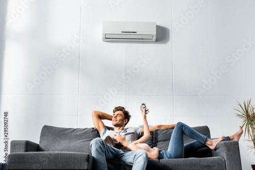 attractive girlfriend switching on air conditioner and lying on legs of handsome boyfriend photo