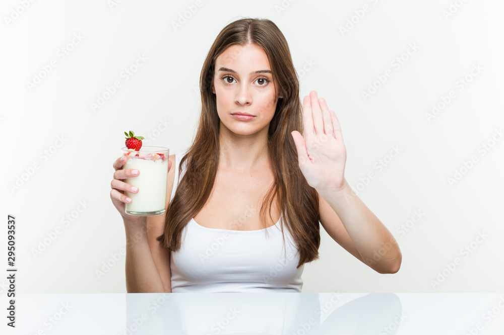 Young caucasian woman holding a smoothie standing with outstretched hand showing stop sign, preventing you. Young caucasian woman holding a smoothie standing with outstretched hand showing stop sign, preventing you.