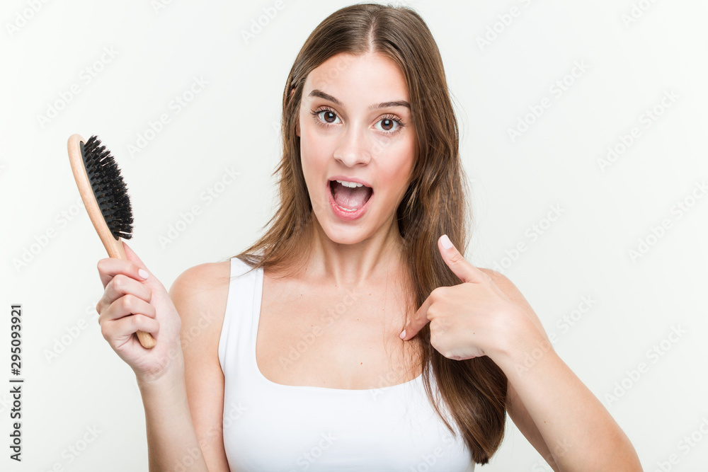 Young caucasian woman holding a hair brush surprised pointing at himself, smiling broadly. Young caucasian woman holding a hair brush surprised pointing at himself, smiling broadly.