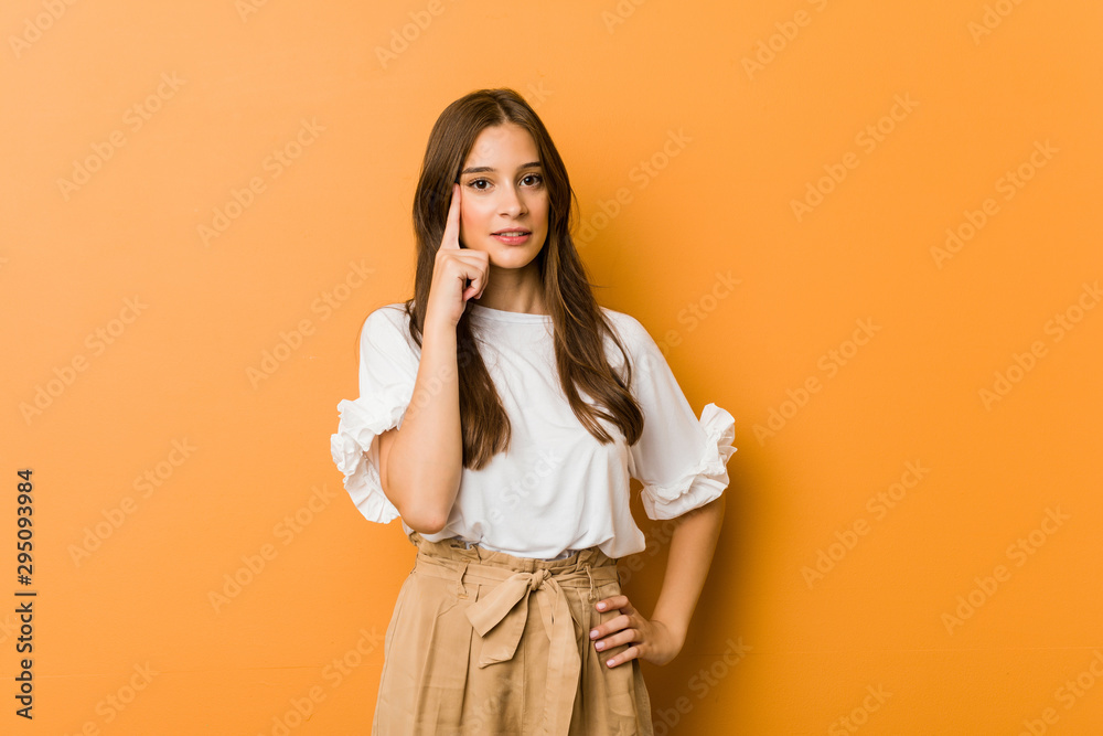 Young caucasian woman pointing temple with finger, thinking, focused on a task. Young caucasian woman pointing temple with finger, thinking, focused on a task.