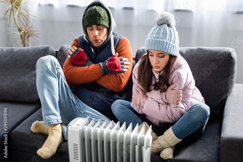 attractive girlfriend and boyfriend in winter outfit warming up near heater