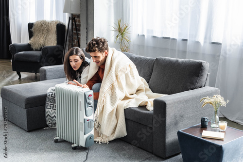 attractive girlfriend and boyfriend covered with blankest warming up near heater