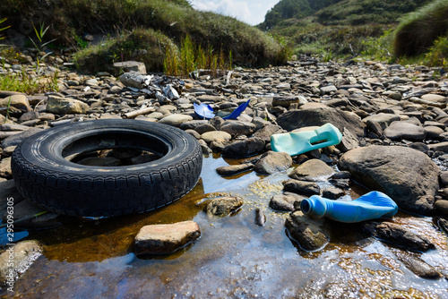 Car tire and plastic bottles in muddy puddle on beach. Beach waste pollution from ocean.