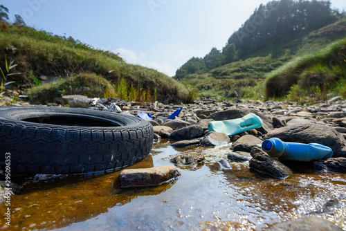 Earth plastics pollution global enviroment emergency. Old car tire in dirty water with plastic bottles and trash.