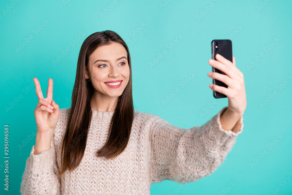 Portrait of charming positive lady making self portrait on her cell phone make v-sign wear knitted jumper isolated over teal turquoise color background Portrait of charming positive lady making self portrait on her cell phone make v-sign wear knitted jumper isolated over teal turquoise color background