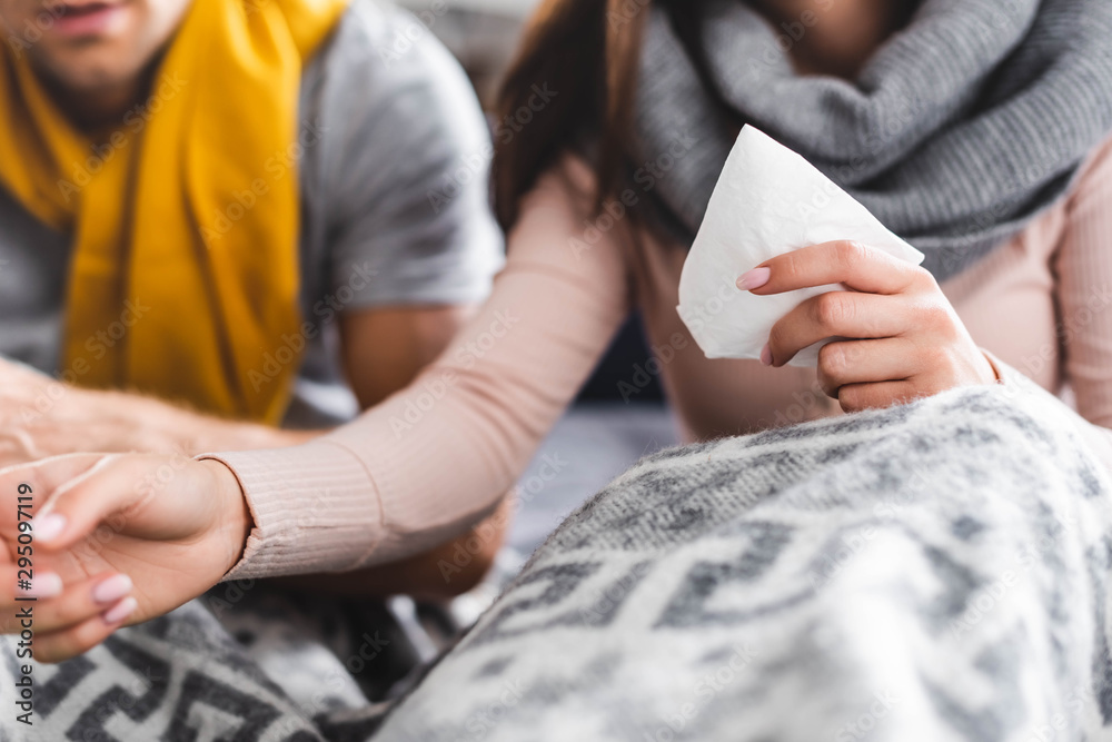 cropped view of sick girlfriend holding napkin in apartment