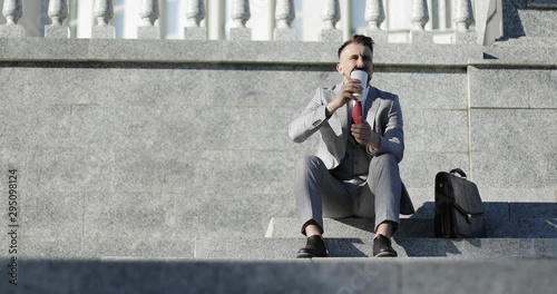 Businessman or lawyer in formal suit with briefcase sits on the steps and drinks coffee. photo