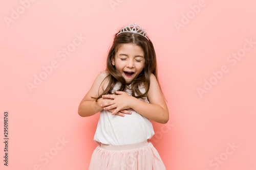 Little girl wearing a princess look laughs happily and has fun keeping hands on stomach.