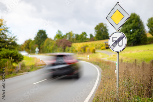 Fototapeta Naklejka Na Ścianę i Meble -  A yellow square sign on the main road and a round white sign. End of the speed limit of 50 kilometers per hour on a German highway. A car drives past high speed.