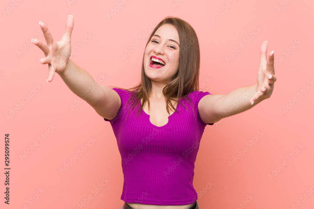Young hispanic woman against a pink wall feels confident giving a hug to the camera.
