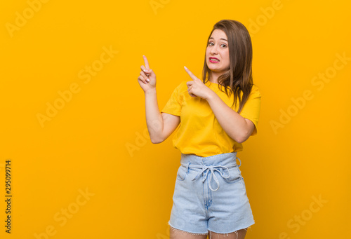 Young woman teenager wearing a yellow shirt shocked pointing with index fingers to a copy space.